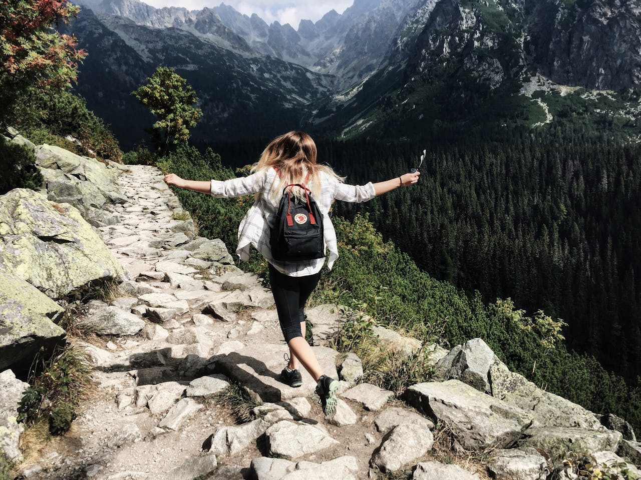 who-we-are Woman hikes along rocky path in Vysoké Tatry, Slovakia. Embracing nature and freedom.