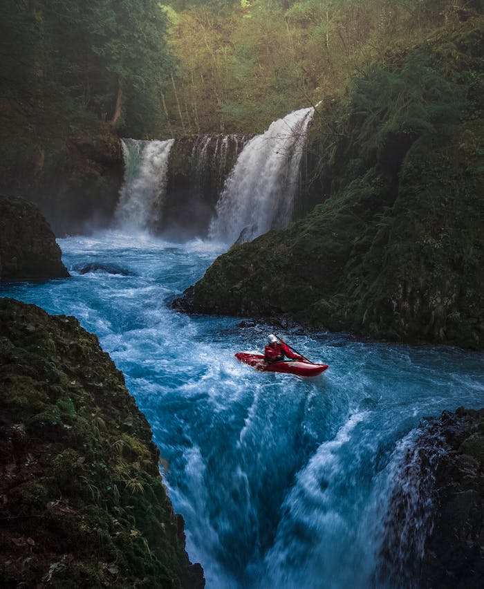 services-03 Dramatic scene of a man kayaking down waterfall surrounded by lush forest.