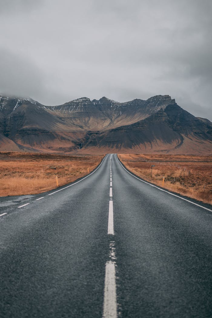 about-us A scenic empty road stretches into snow-capped mountains under cloudy skies, offering a sense of adventure and tranquility.