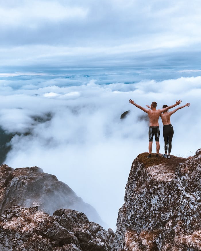 services-04 Two hikers stand on a rocky cliff, embracing the expansive mountain view and clouds, symbolizing freedom and exploration.
